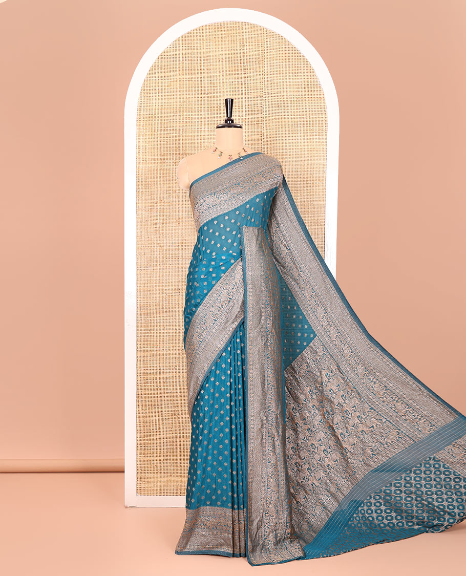 Blue Semi-Banaras Khaddi Georgette Embellished with Zari Buttas All Over Its Body, Subtly Sparkled Traditional Border of Rudraksham, Elephant, and Floral Vine Designs, Pallu of a Herd of Elephants, and Paired with a Matching Blouse