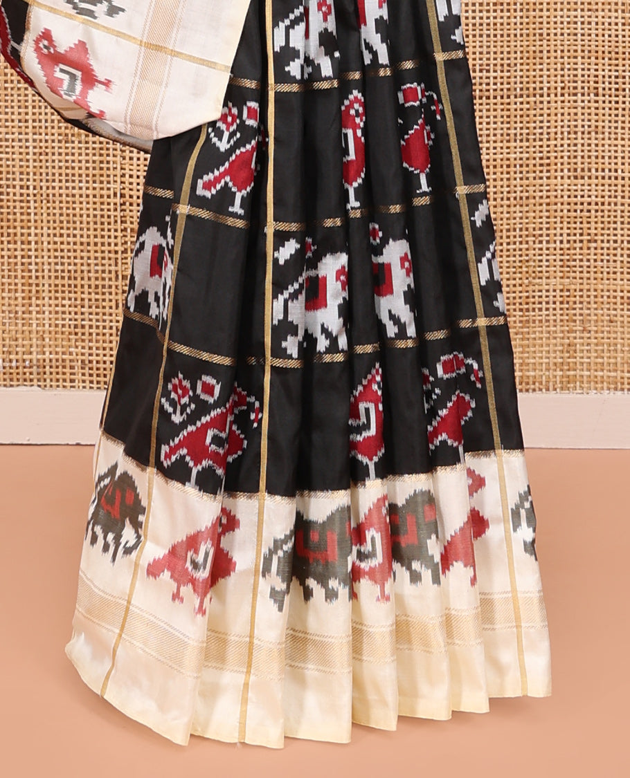 Black Ikkat Silk Saree, Impeccably Styled with Patola-Style Parrot-Elephant Butta Enclosed Checks on Its Body, Complemented by a Contrast Patola-Style Parrot-Elephant Butta Enclosed Border, Pallu of the Same Motifs, and Paired with a Contrast Blouse