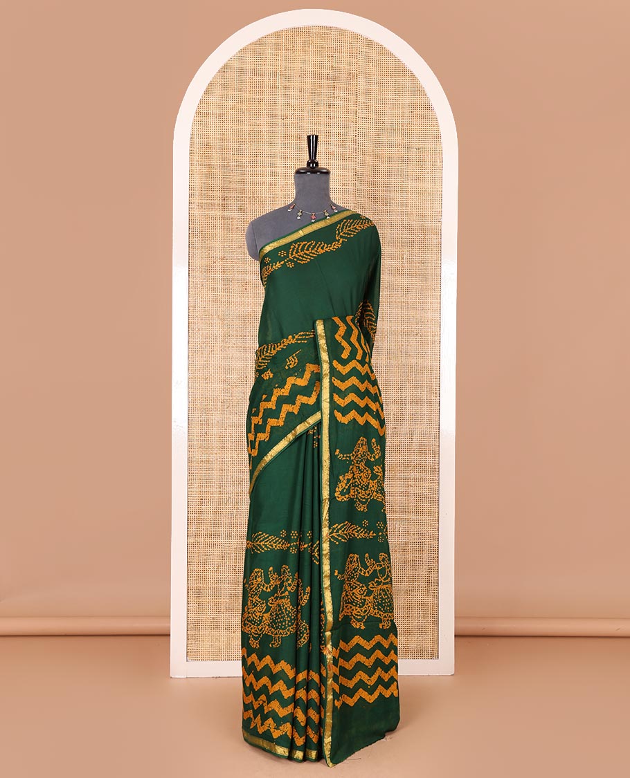 Green wax batik-style zig-zag printed pure cotton saree, gold zari piping border, human figurines batik printed pallu, and a matching blouse