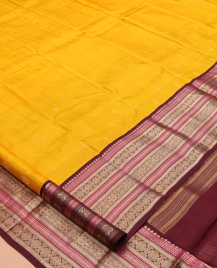Yellow Vasundhara Silk Saree Subtly Sparkled with Buttas Enclosed Checks All Over Its Body, Complemented by Contrast Border of Rekku, Chakram, and Jada Nagam Designs, a Grandly Woven Pallu of Intricate Mughal Designs, and Paired with a Contrast Blouse