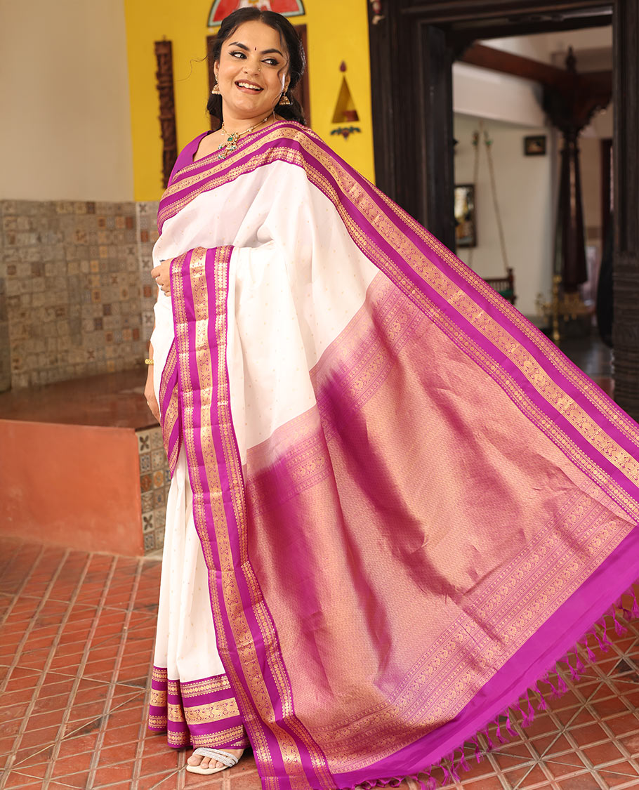 White Vasundhara Silk Saree Elegantly Embellished with Zari Buttas, Complemented by a Varisai Pettu Border Featuring Rekku, Muthu, Banaras, Rudraksham, and Mayil Designs, Majestically Woven with a Zari-Designed Pallu, and Paired with a Contrast Blouse