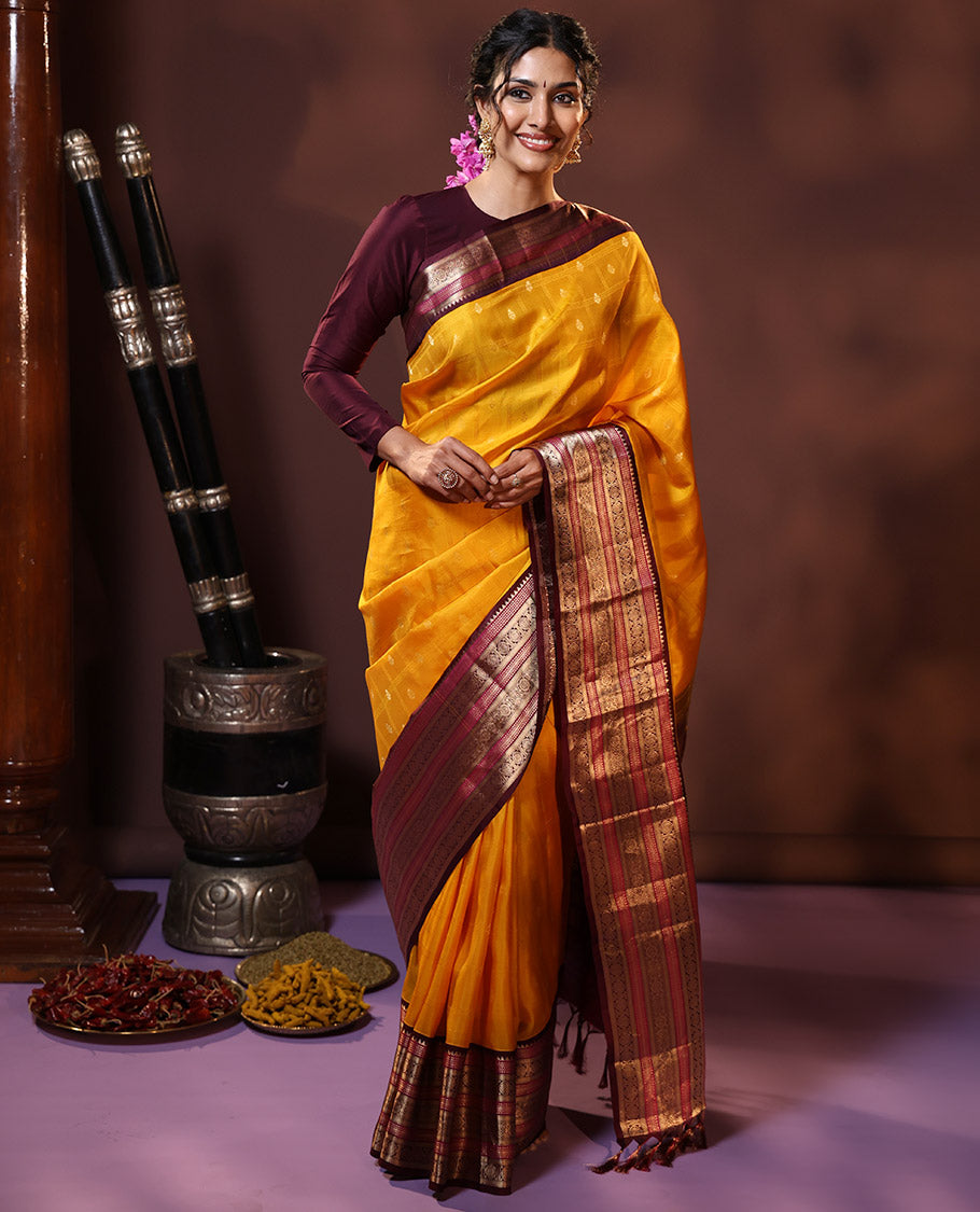 Yellow Vasundhara Silk Saree Subtly Sparkled with Buttas Enclosed Checks All Over Its Body, Complemented by Contrast Border of Rekku, Chakram, and Jada Nagam Designs, a Grandly Woven Pallu of Intricate Mughal Designs, and Paired with a Contrast Blouse