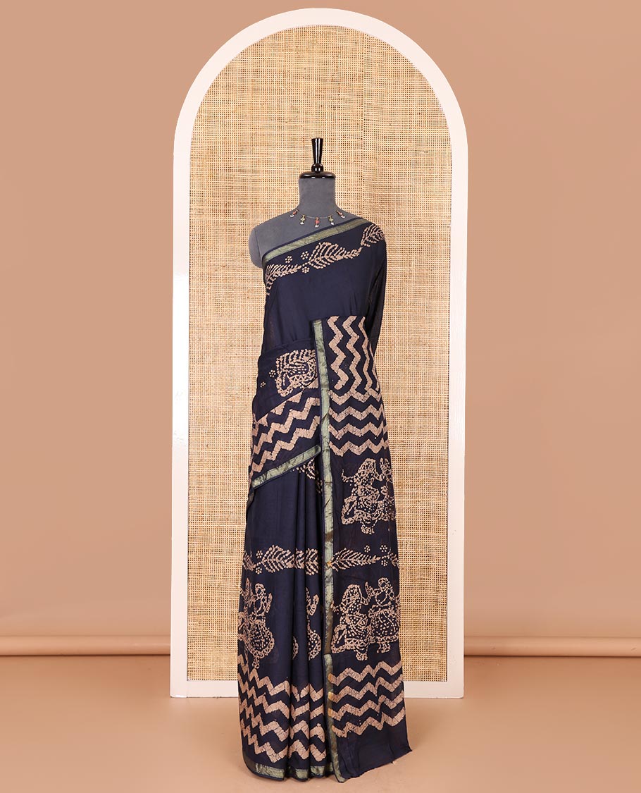 Navy blue wax batik-style zig-zag printed pure cotton saree, gold zari piping border, human figurines batik printed pallu, and a matching blouse