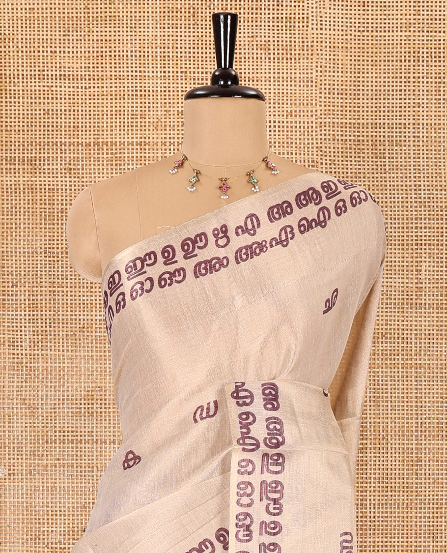 Cream-magenta Malayalam letter printed tissue saree, self-border and pallu steeped with Malayalam letter motifs, and a contrast plain blouse