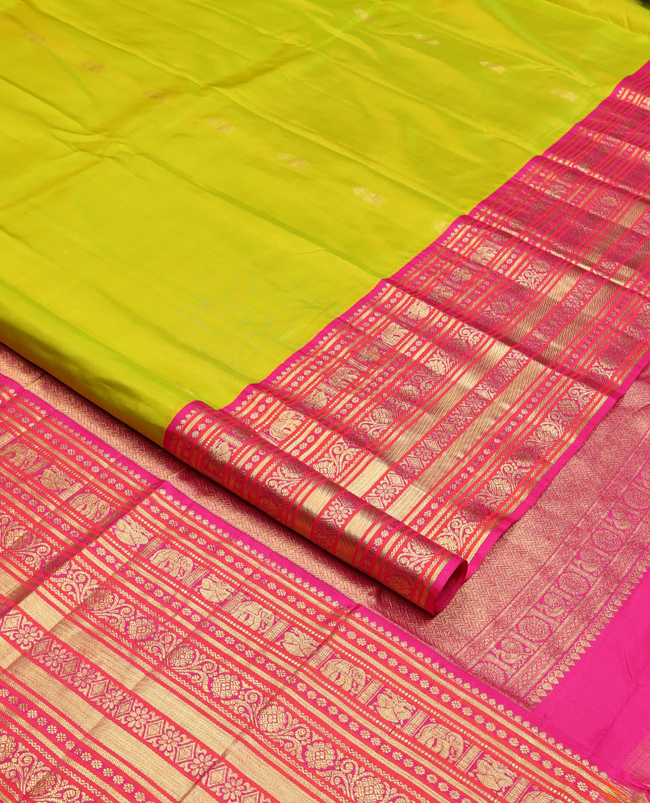 Green Vasundhara Silk Saree, Delicately Woven with Zari Buttas All Over Its Body, Complemented by Contrast Border of Thilakam Mokku, Kamalam, Iruthalai Pakshi, Yaanai, and Kamalam Designs, Vanki Design Pallu and Paired with a Contrast Blouse