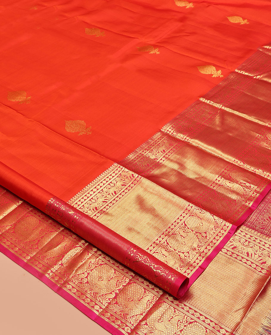 Orange Kanchipuram Silk Saree, Bedecked with Zari Buttas All Over Its Body, Complemented by a Contrast Border of Manga Mokku, Poun, Yaanai, and Mayil Designs, Grand Pallu of Kodi Visiry Designs, and Paired with a Contrast Blouse
