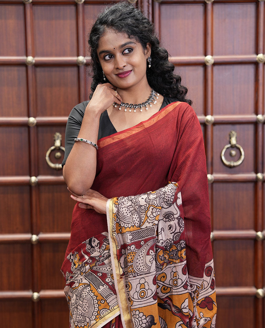 Maroon Kota Cotton Saree, Artfully Decked Up with Kalamkari-Style Human Figurines Printed on the Body, Subtle Piping Border, Pallu Pictures Kalamkari-Style Flora-Fauna Motifs, and Paired with a Contrast-Printed Blouse