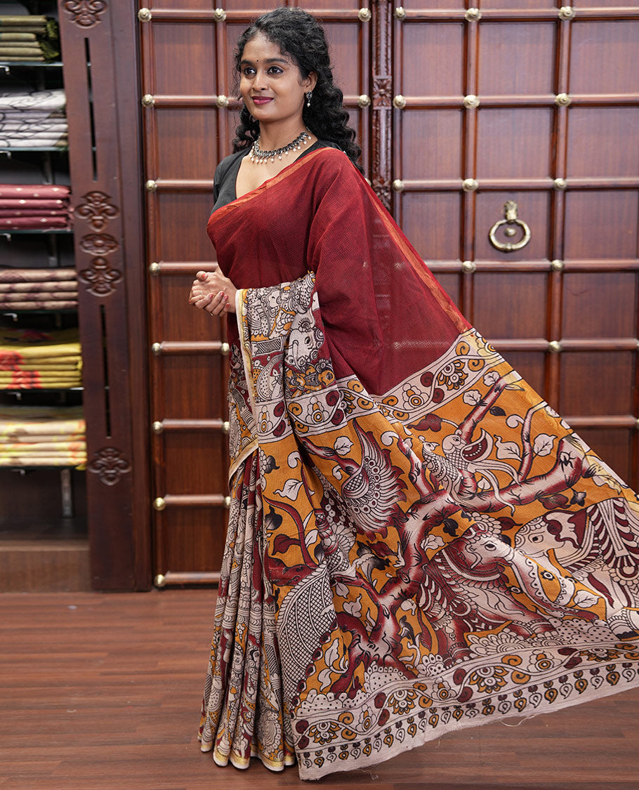 Maroon Kota Cotton Saree, Artfully Decked Up with Kalamkari-Style Human Figurines Printed on the Body, Subtle Piping Border, Pallu Pictures Kalamkari-Style Flora-Fauna Motifs, and Paired with a Contrast-Printed Blouse