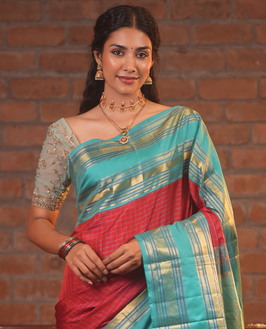 Tomato Red and Blue Vasundhara Silk Saree, Subtly Sparkled With Pattu Nool Kattam On Its Body, Complemented by Contrast Rettai Pettu Border of Salngai, Muthu, Neli, Rudraksham, and Dhavana Kodi Designs, Grand Pallu and Paired with a Contrast Blouse