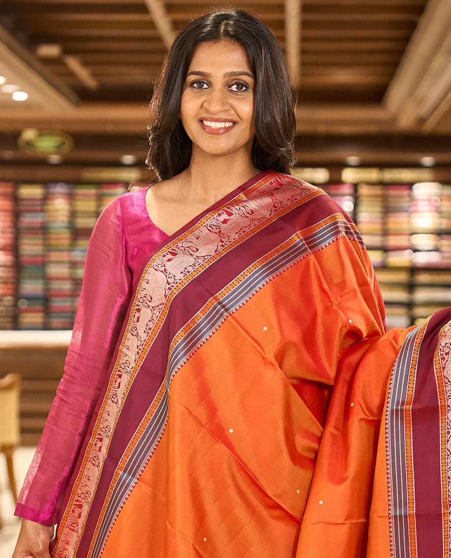 Orange thread buttas Kanchipuram silk saree, contrast rettai pettu border of rekku, rudraksham, yaanai, and Pichwai cow designs, and pallu features Vrishabha Kunjara design