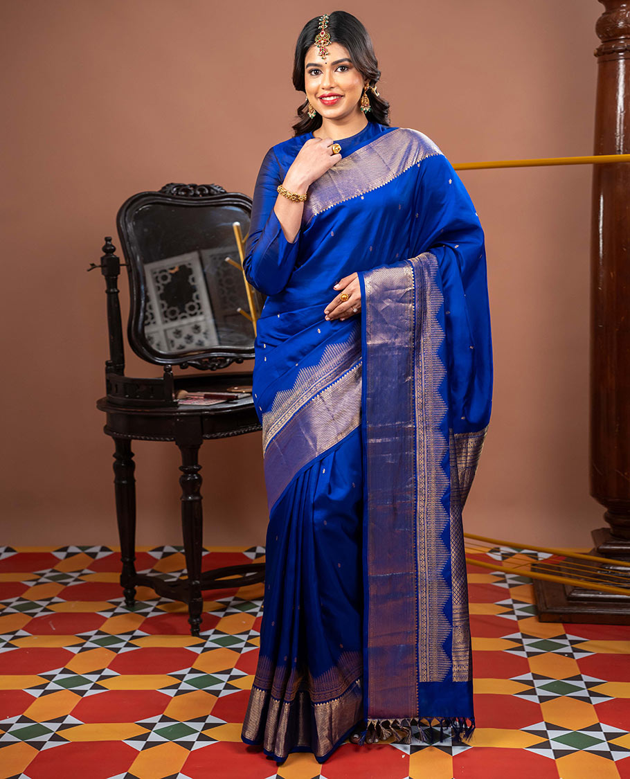 Blue Vasundhara Silk Saree Gleamed with Zari Buttas All Over Its Body, Highlighted with a Zari Border of Thilakam Mokku, Muthu, Cross Kamalam, and Mayil Kann Designs, Grand Pallu of Jaal Design, and Paired with a Matching Blouse
