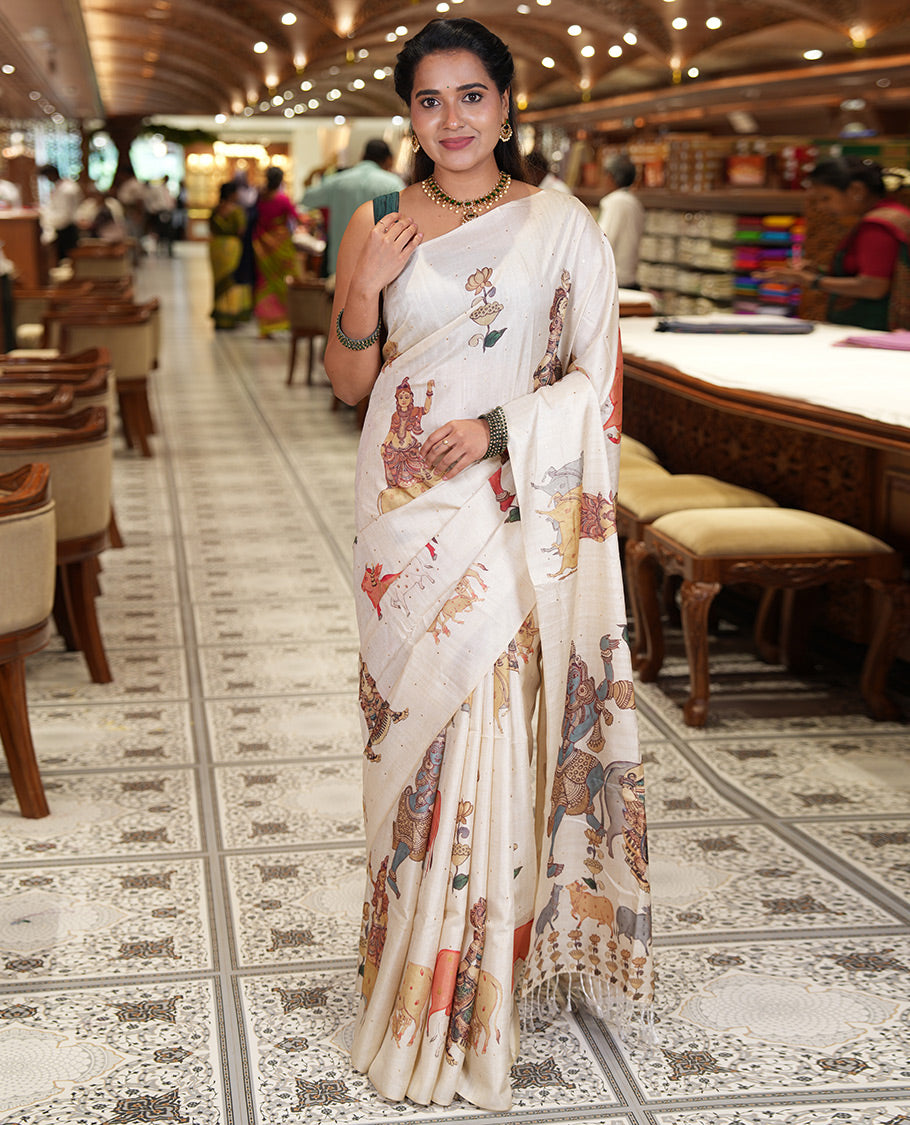 Borderless Cream Semi-Tussar Saree, Artfully Printed with Ancient Human Figurines, Floral, and Pichwai Cow on Its Body, Highlighted by Kalamkari-Style Human Motifs Printed Pallu, and Paired with a Matching Pichwai Cow Printed Blouse
