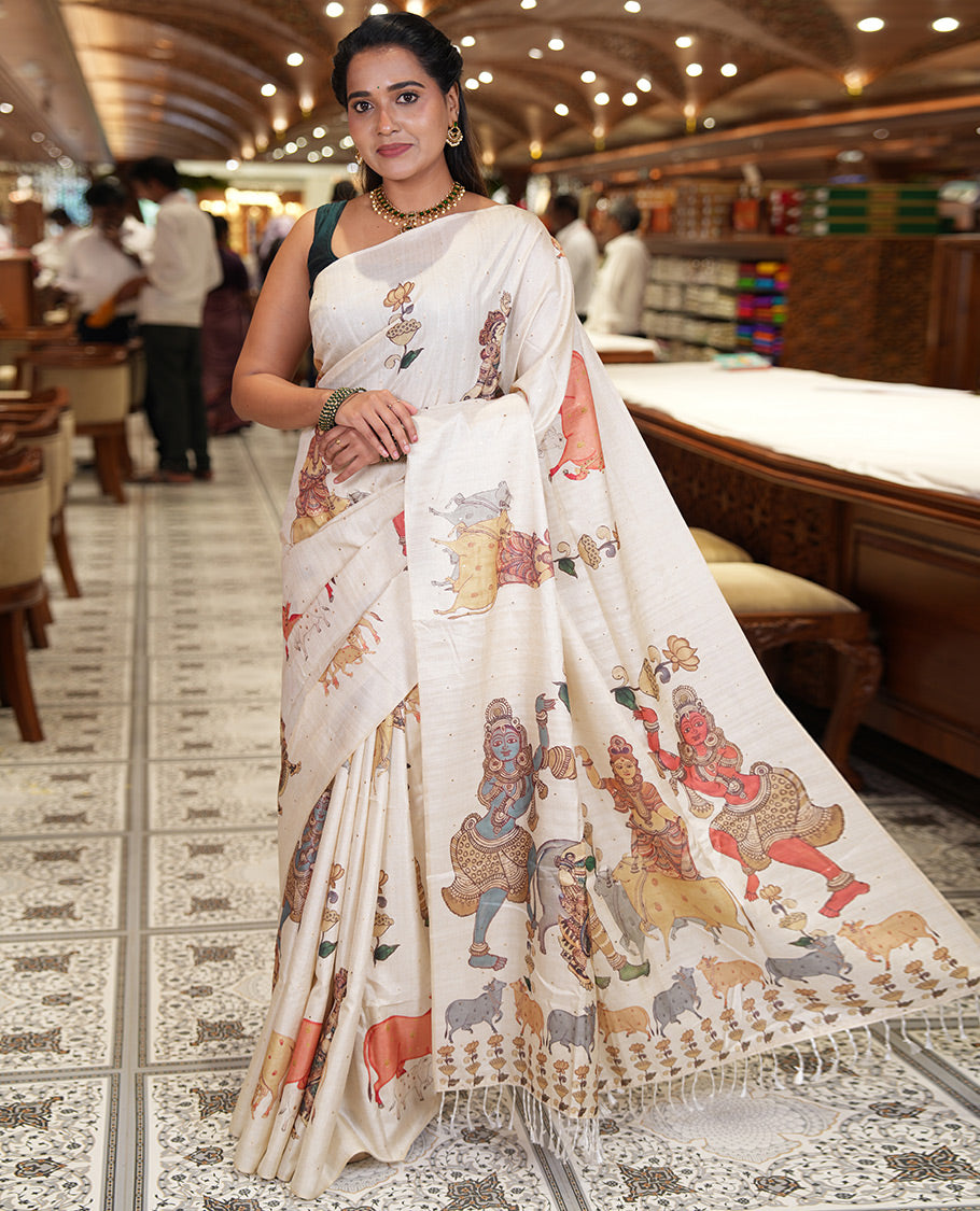 Borderless Cream Semi-Tussar Saree, Artfully Printed with Ancient Human Figurines, Floral, and Pichwai Cow on Its Body, Highlighted by Kalamkari-Style Human Motifs Printed Pallu, and Paired with a Matching Pichwai Cow Printed Blouse