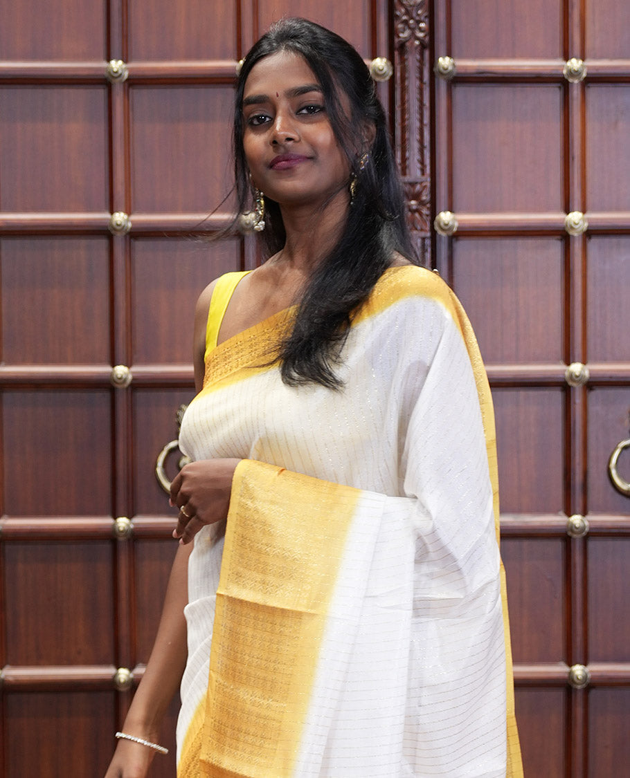White and Yellow Dola Silk Saree Decked Up with Vertical Zari Stripes All Over the Body, Complemented by a Contrast Border of Traditional Zari Designs, Self-Pallu of Stripes, and Paired with a Contrast Blouse