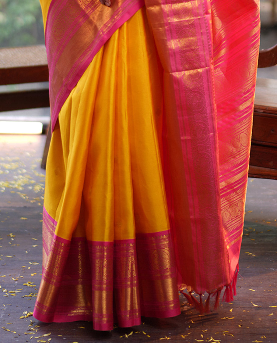 Mango Yellow Vasundhara Silk Saree, Subtly Sparkled with Sparse Stripes and Zari Buttas, Complemented by a Contrast Border of Thilakam, Banaras, Muthu, and Round Mayil Designs, Pallu Steeped with Traditional Designs, and Paired with a Contrast Blouse
