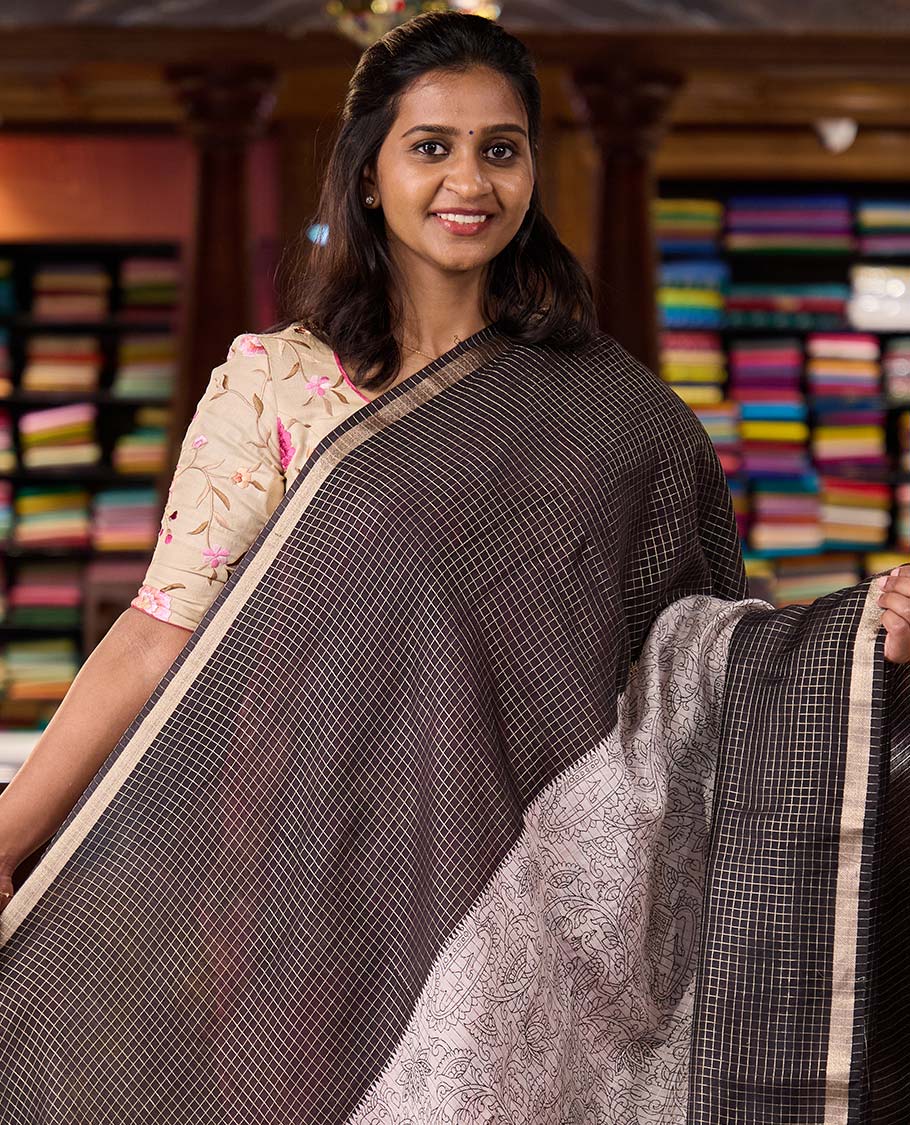 Black and beige half-and-half style Muga silk saree adorned with zari micro-checks, and kalamkari flora-fauna prints, zari piping border, and zari striped pallu