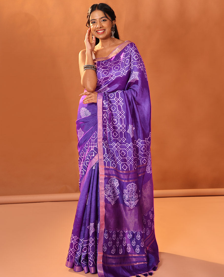Purple Banana Pith Gleamed Up with Batik-Style Star and Kolam Motifs Printed All Over Its Body, Subtly Woven Zari Piping Border, Pallu Depicts Floral Motifs Block Print, and Gleaming Zari Stripes, and Paired with a Contrast Blouse