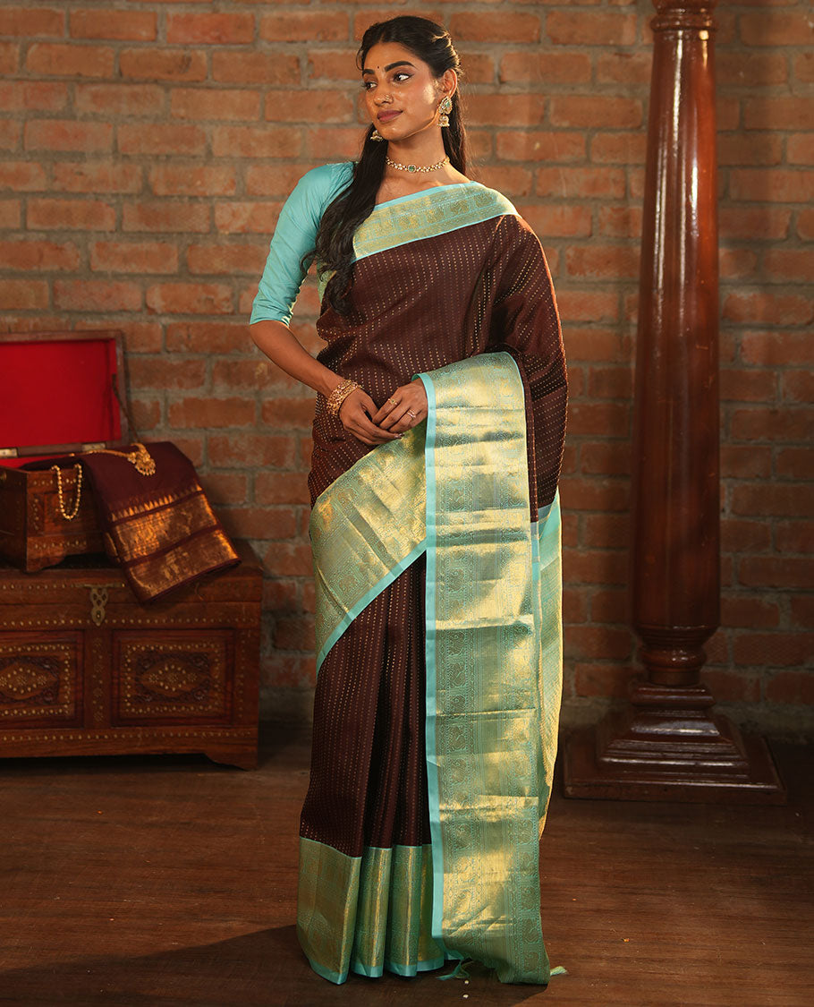 Brown Vasundhara Silk Saree Delicately Woven with Zari Buttas, Highlighted with a Contrast Border of Cross Kamalam, Mayil, Banaras, Yaanai, and Mayil Kann Designs, Pallu Grandly Woven with Jaal Designs, and Paired with a Contrast Blouse