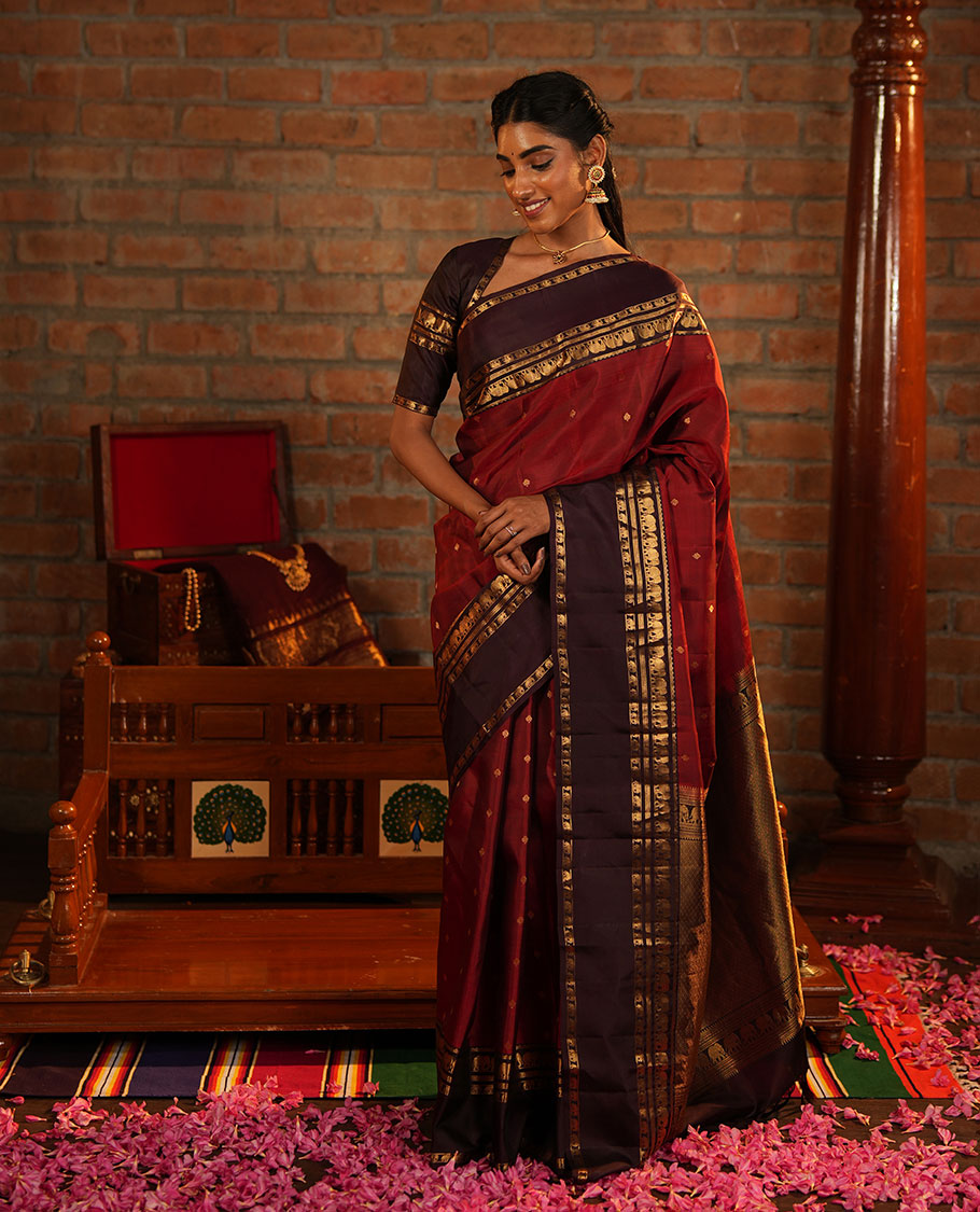 Maroon Vasundhara Silk Saree Decorated with Zari Buttas All Over Its Body, Complemented by a Contrast Rettai Pettu Border Steeped with Yaanai Motifs, Richly Detailed Pallu of Jaal Designs, and Paired with a Contrast Zari Bordered Blouse