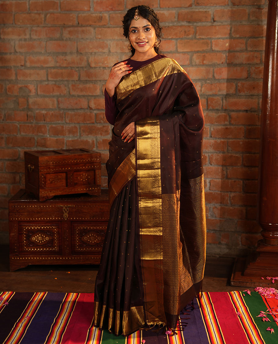 Brown Vasundhara Silk Saree Beautified with Zari Buttas All Over Its Body, Gleamed Up with a Zari Border of Thilakam Mokku, Kathir, Rudraksham, and Arumbu Manga Designs, Majestically Detailed Pallu of Jaal Designs, and Comes with a Matching Blouse
