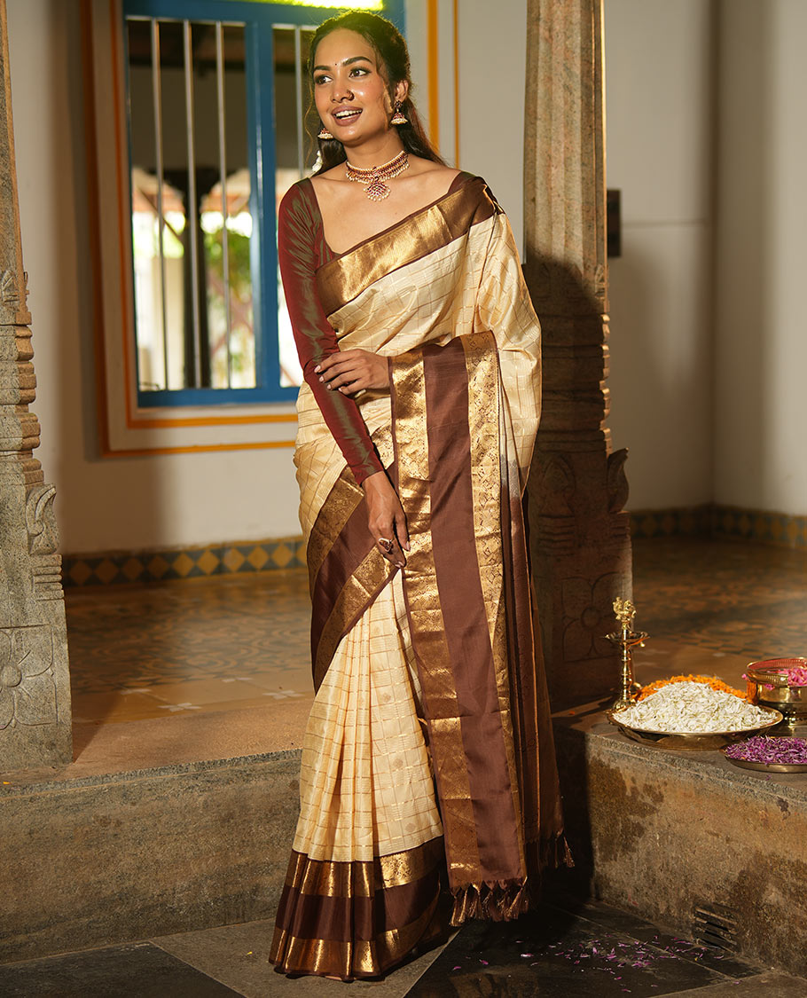 Cream Vasundhara Silk Saree, Enthralled with Zari Buttas Enclosed Checks All Over Its Body, Complemented by a Contrast Rettai Pettu Border of Muthu, Banaras, and Iruthalai Pakshi Designs, a Grand Pallu, and Paired with a Contrast Blouse