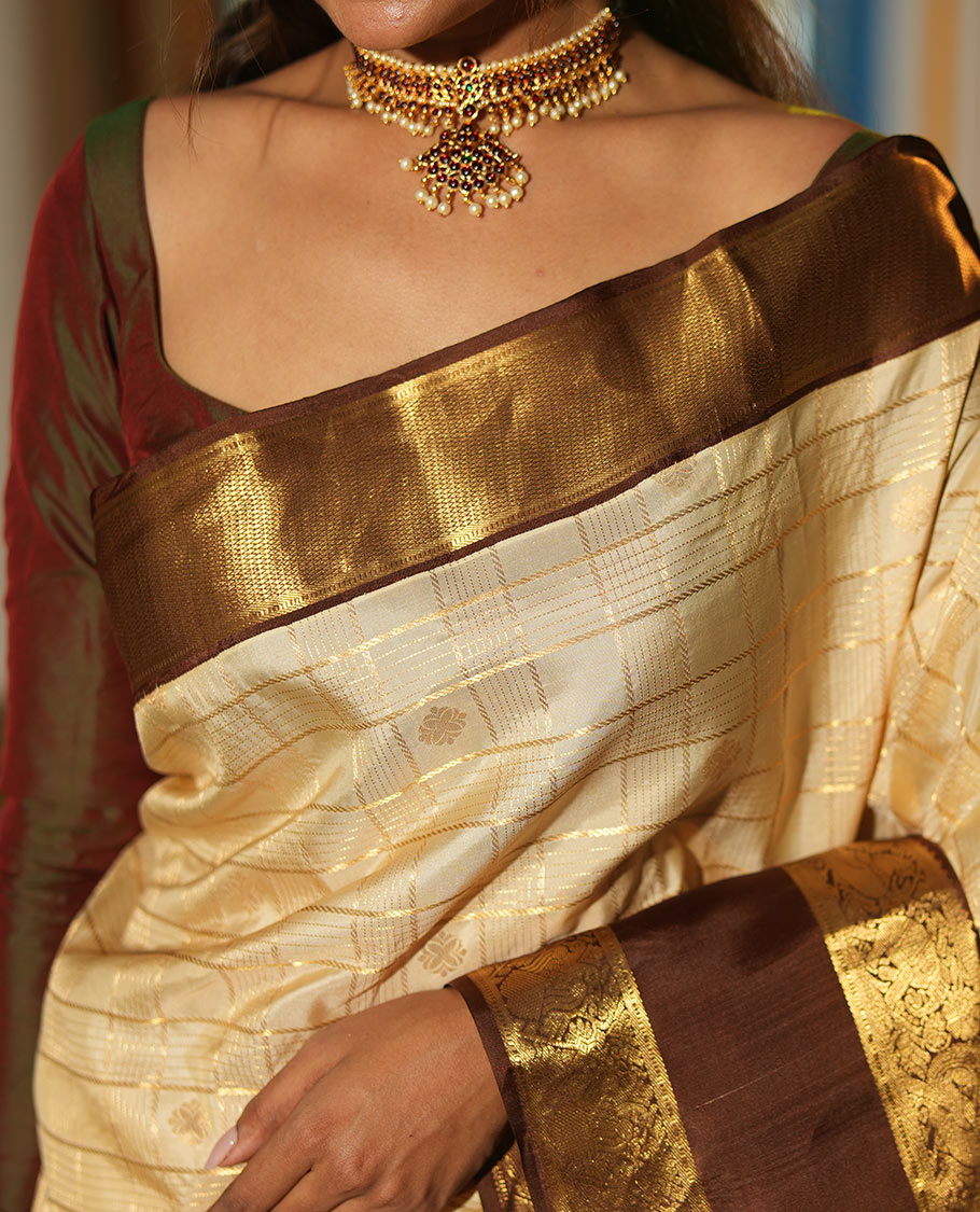 Cream Vasundhara Silk Saree, Enthralled with Zari Buttas Enclosed Checks All Over Its Body, Complemented by a Contrast Rettai Pettu Border of Muthu, Banaras, and Iruthalai Pakshi Designs, a Grand Pallu, and Paired with a Contrast Blouse