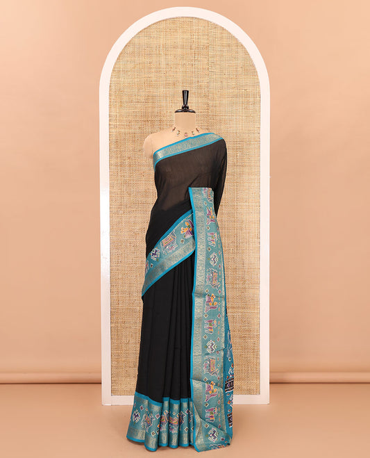 Black embossed moss chiffon saree, contrast zari and colorfully printed border and pallu of human figurines and Pichwai cows, and embossed blouse