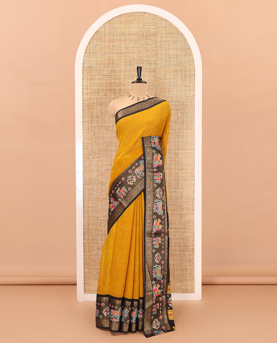 Mustard embossed moss chiffon saree, contrast zari and colorfully printed border and pallu of human figurines and Pichwai cows, and embossed blouse