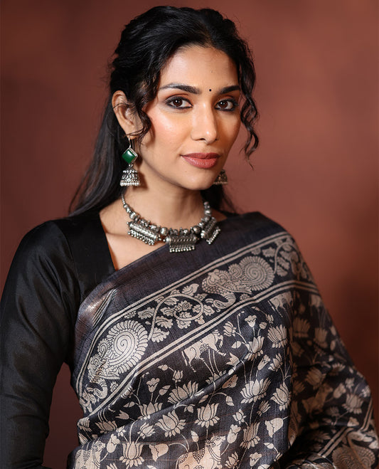 Black Tussar Saree Artfully Printed with Pichwai Cow and Lotus Motifs All Over Its Body, Subtly Made Self-Border of Kalamkari Floral-Peacock Print, Pallu Mirroring Pichwai Cow-Lotus Print, and Paired with a Plain Blouse