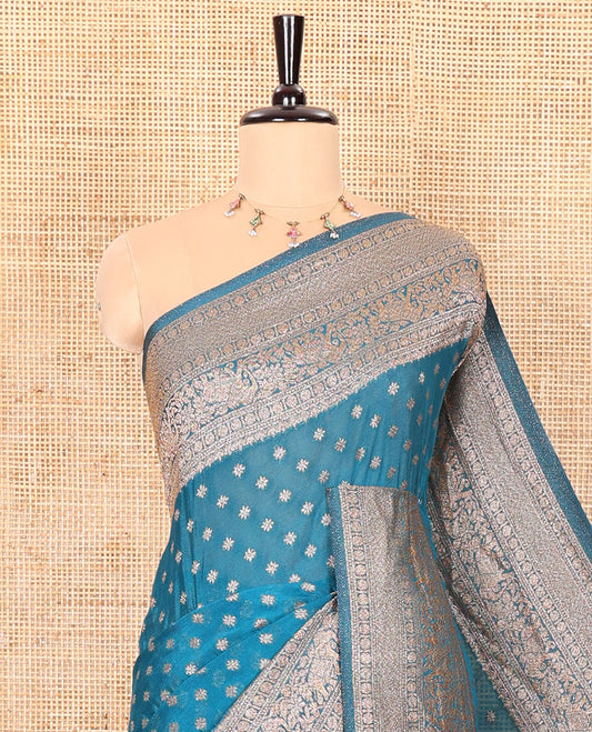 Blue Semi-Banaras Khaddi Georgette Embellished with Zari Buttas All Over Its Body,  Subtly Sparkled Traditional Border of Rudraksham, Elephant, and Floral Vine Designs, Pallu of a Herd of Elephants, and Paired with a Matching Blouse