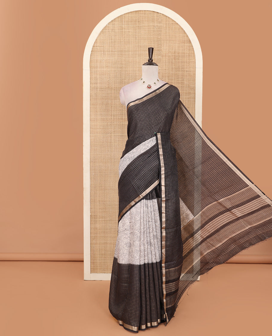 Black and beige half-and-half style Muga silk saree adorned with zari micro-checks, and kalamkari flora-fauna prints, zari piping border, and zari striped pallu