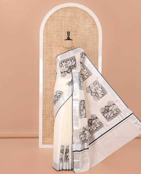 Half-White Kerala Cotton Saree, Artfully Detailed with Kalamkari-Style Elephant Motifs on Its Body, Highlighted by Zari Border, Pallu Pictures the Same Print, and Paired with a Matching Blouse