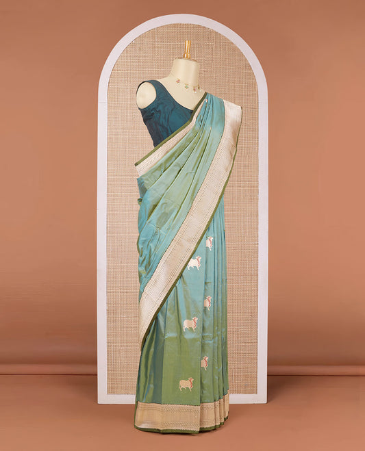 Green dual-shaded katan silk saree with pichwai cow motifs, contrast zari border & pallu features intricate designs