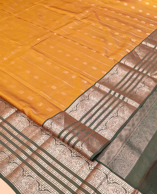 Mustard Vasundhara Lite Silk Mix Saree, Richly Detailed with Zari Buttas and Stripes All Over Its Body Complemented by Contrast Border of Thilakam Mokku, Rudraksham, and Mayil Designs, Grand Jaal Pallu, and Paired with a Contrast Blouse