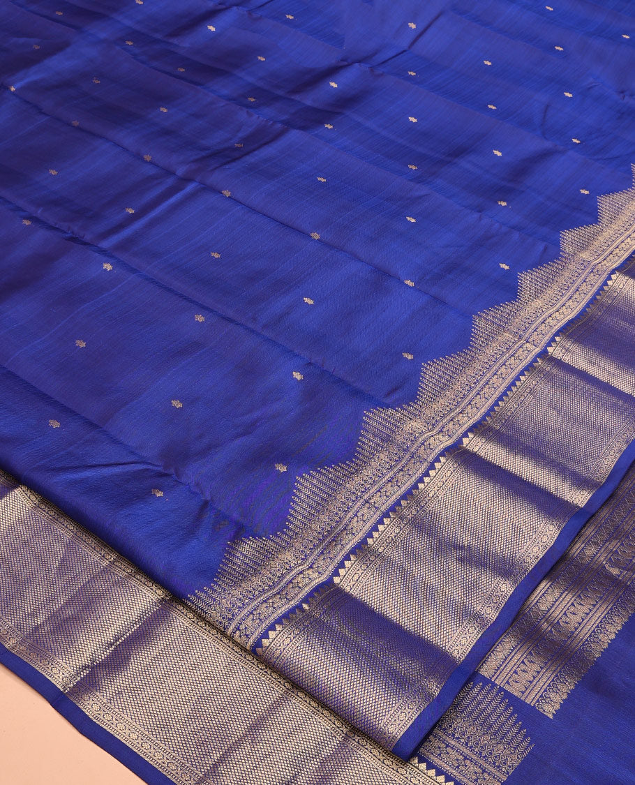 Blue Vasundhara Silk Saree Gleamed with Zari Buttas All Over Its Body, Highlighted with a Zari Border of Thilakam Mokku, Muthu, Cross Kamalam, and Mayil Kann Designs, Grand Pallu of Jaal Design, and Paired with a Matching Blouse