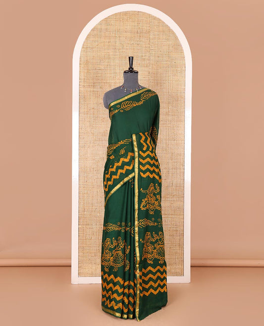 Green wax batik-style zig-zag printed pure cotton saree, gold zari piping border, human figurines batik printed pallu, and a matching blouse