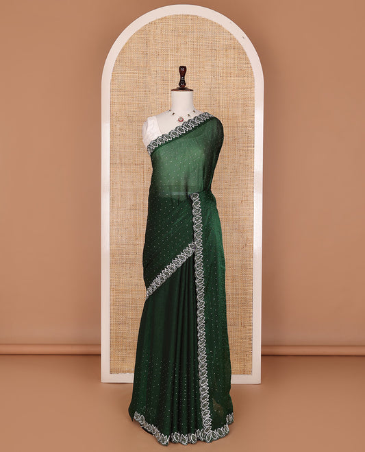 Deep forest green designer saree features gleaming crystal stone embedded all-over its body, scallop leaf motifs embroidered border