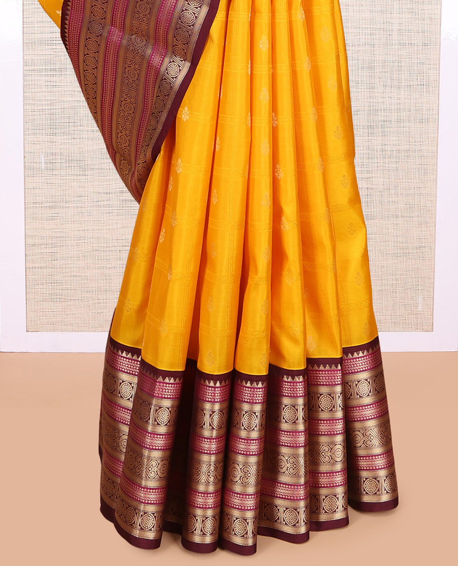 Yellow Vasundhara Silk Saree Subtly Sparkled with Buttas Enclosed Checks All Over Its Body, Complemented by Contrast  Border of Rekku, Chakram, and Jada Nagam Designs, a Grandly Woven Pallu of Intricate Mughal Designs, and Paired with a Contrast Blouse
