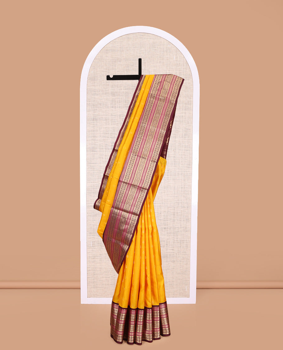 Yellow Vasundhara Silk Saree Subtly Sparkled with Buttas Enclosed Checks All Over Its Body, Complemented by Contrast  Border of Rekku, Chakram, and Jada Nagam Designs, a Grandly Woven Pallu of Intricate Mughal Designs, and Paired with a Contrast Blouse