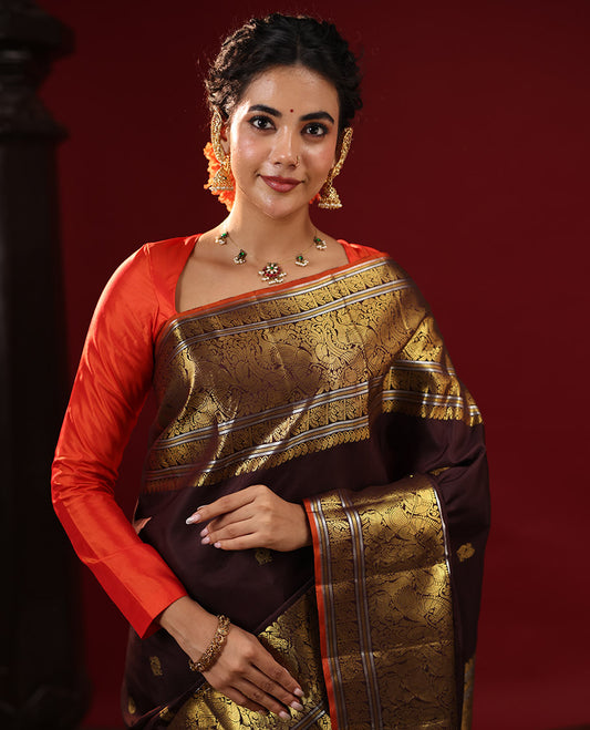 Brown Kanchipuram Silk Saree Embellished with Zari Buttas All Over the Body, Complemented by Zari Border of Manga Mokku, Banaras, Muthu, Mayil, Kuthirai, and Yaali Designs, Gracefully Decked Up Pallu, and Paired with a Matching Blouse