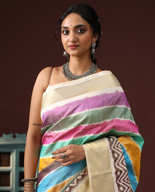 Multi-Color Ikkat Silk Saree Adorned with Kaleidoscope-Colored Stripes All Over Its Body, Complemented by Contrast Chevron Zari Border, Pallu Depicts Ikkat Woven Chevron Patterns, and Paired with a Matching Blouse