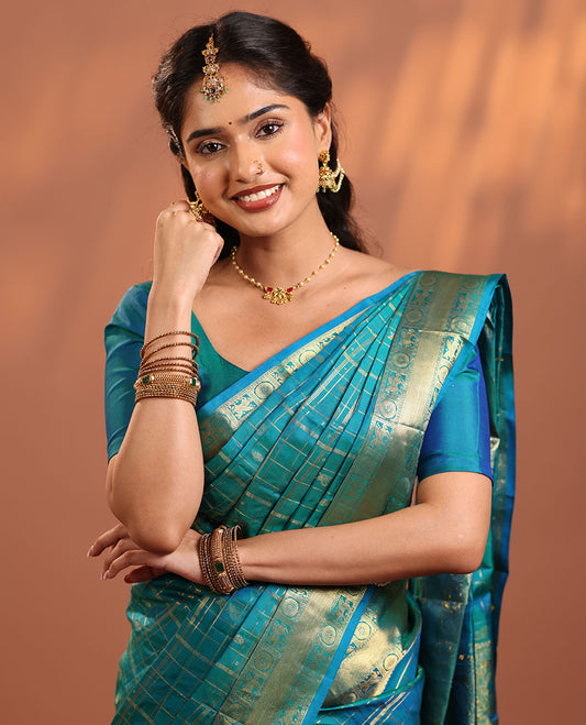 Peacock Blue Vasundhara Silk Saree Gleamed Up with Zari Buttas Enclosed in Zari Checks, Featuring a Zari Border of Kuthirai and Chakra Designs, Pallu Complemented by Rich Zari Weave, and a Matching Blouse