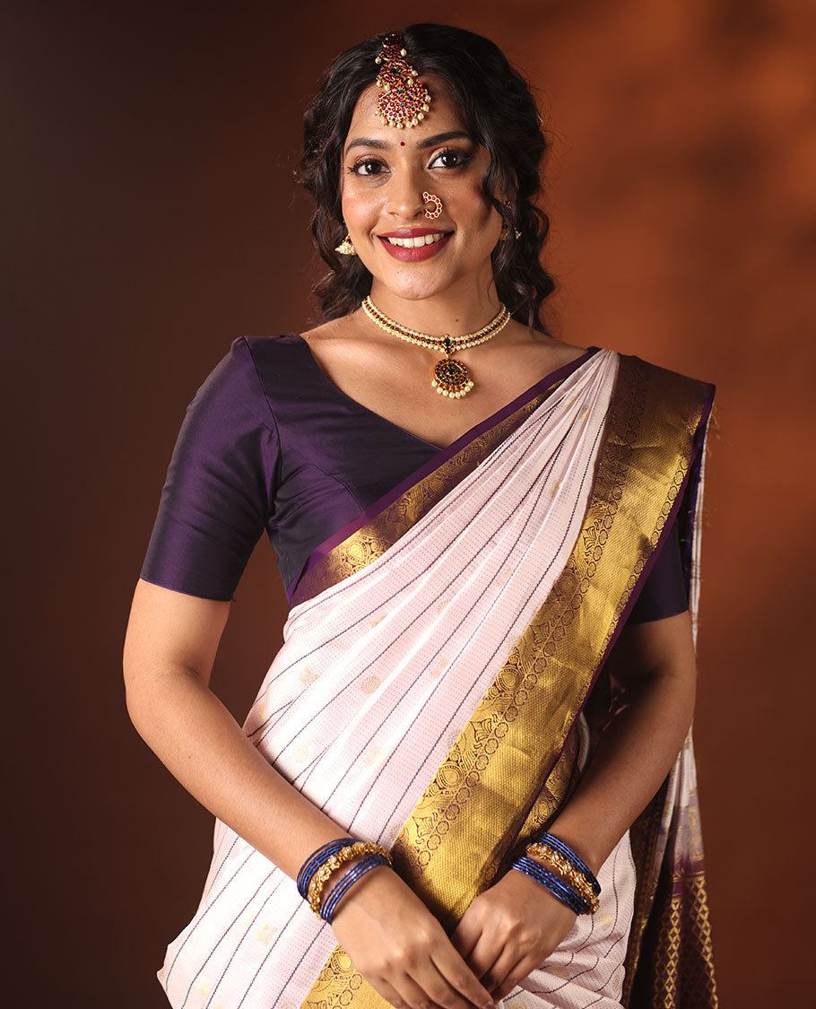 White silk saree adorned with Mayil Chakram, Neli, and Muthu stripes, featuring a contrast border with Laddu Kamalam, Mayil, Yaali, and Mayil Kann designs, along with a Jaal design pallu