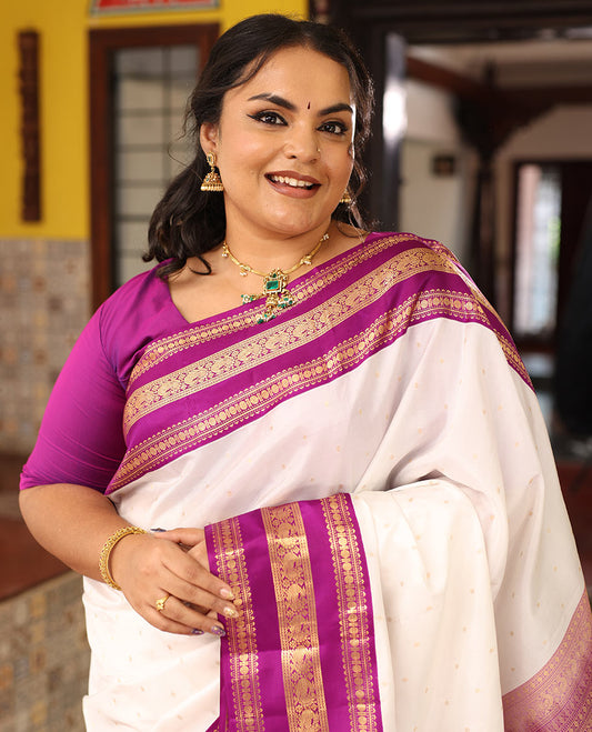 White Vasundhara Silk Saree Elegantly Embellished with Zari Buttas, Complemented by a Varisai Pettu Border Featuring Rekku, Muthu, Banaras, Rudraksham, and Mayil Designs, Majestically Woven with a Zari-Designed Pallu, and Paired with a Contrast Blouse