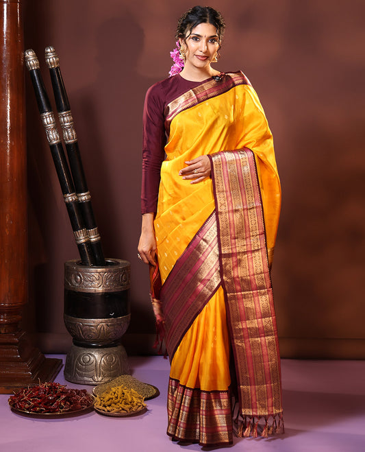 Yellow Silk Saree Subtly Sparkled with Buttas Enclosed Checks All Over Its Body, Complemented by Contrast  Border of Rekku, Chakram, and Jada Nagam Designs, a Grandly Woven Pallu of Intricate Mughal Designs, and Paired with a Contrast Blouse