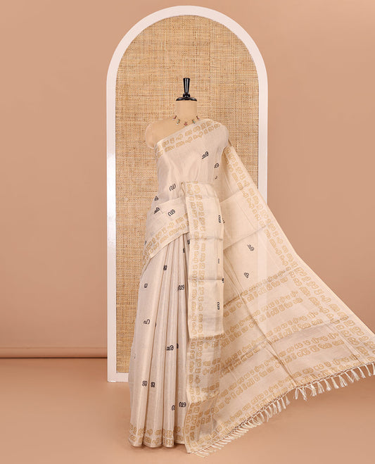 Cream-mustard Malayalam letter printed tissue saree, self-border and pallu steeped with Malayalam letter motifs, and a contrast plain blouse