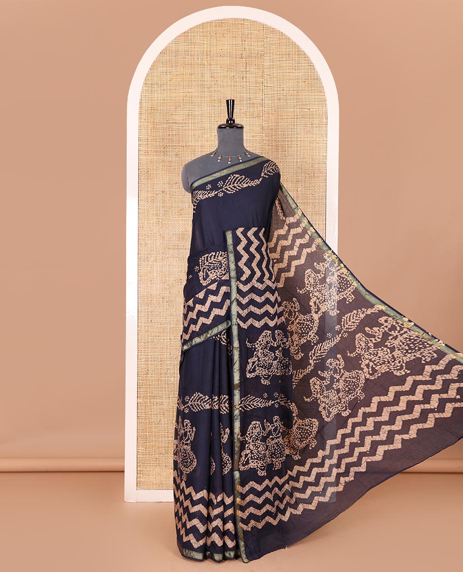 Navy blue wax batik-style zig-zag printed pure cotton saree, gold zari piping border, human figurines batik printed pallu, and a matching blouse