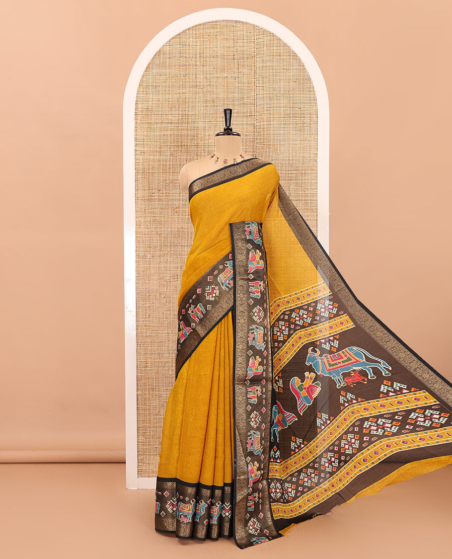 Mustard embossed moss chiffon saree, contrast zari and colorfully printed border and pallu of human figurines and Pichwai cows, and embossed blouse