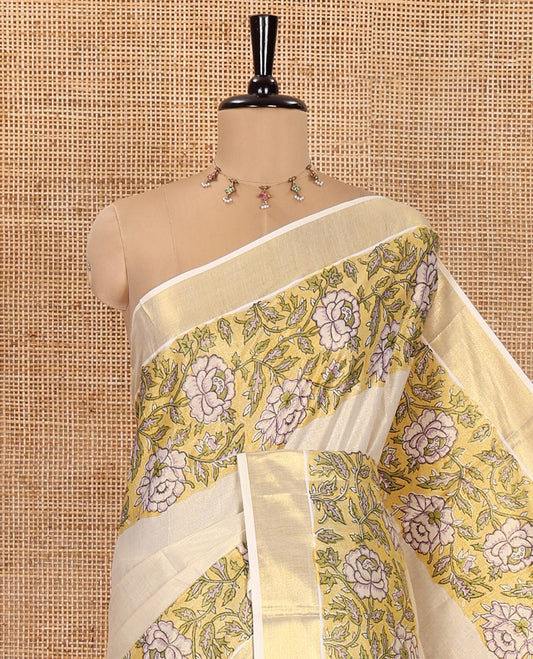 Cream Kerala Tissue Saree, Enriched with Floral Vine Motifs Printed on Its Body, Gleaming Golden Zari Border, Pallu Mirrors the Same Floral Vine Print, and Paired with a Matching Printed Blouse