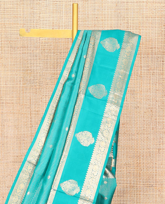 Blue Vasundhara Silk Saree Decked Up with Zari Buttas All Over Its Body, Highlighted by a Zari Border of Thilakam Mokku, Poun, Mayil, and Zari Designs, Grand Pallu of Butta Enclosed Checks, and Paired with a Matching Blouse